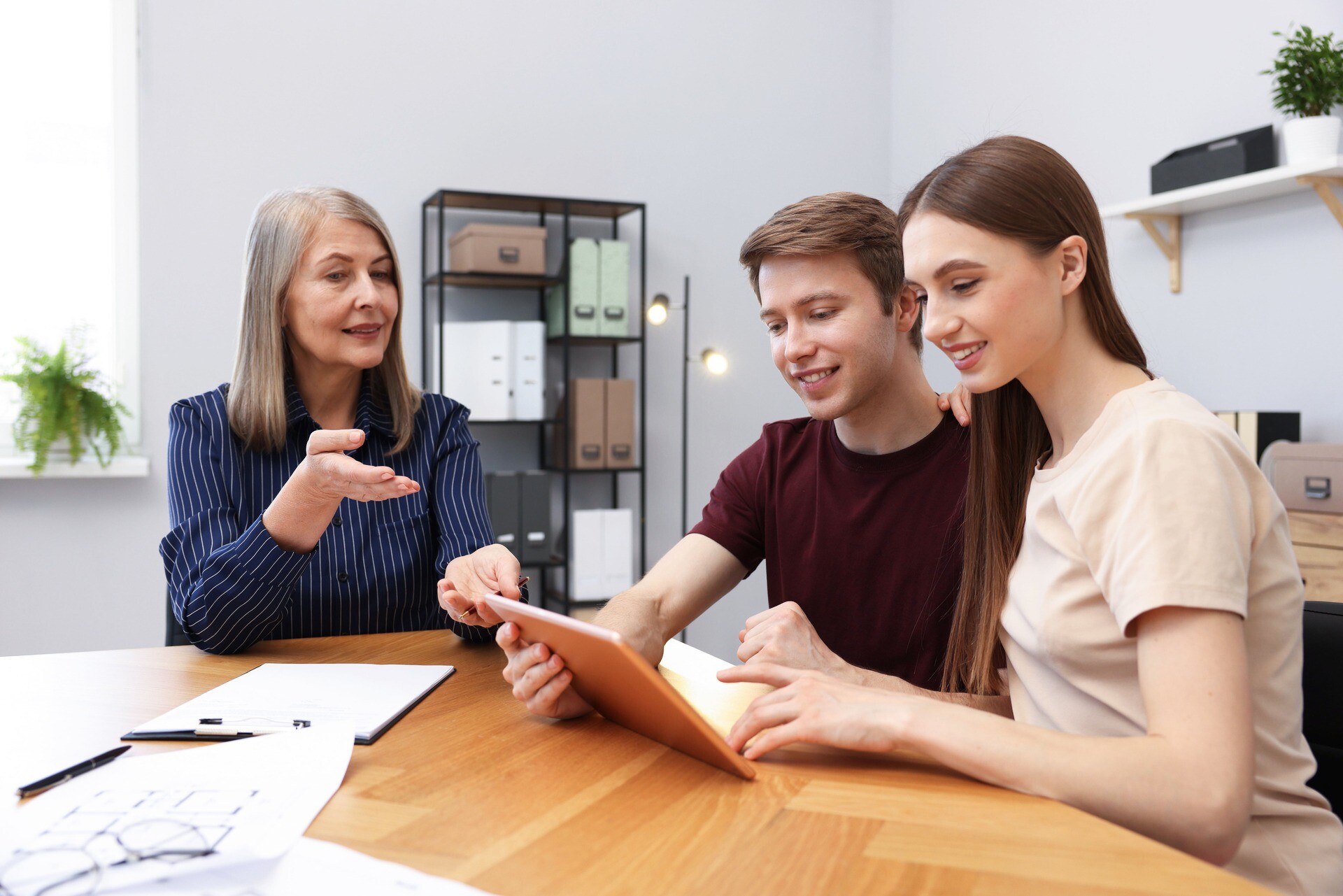 Drei Personen sehen sich am Tisch gemeinsam ein Tablet an.