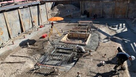 Arbeiter stellen Bewehrungsstäbe und Holzschalungen auf einer Baustelle auf.
