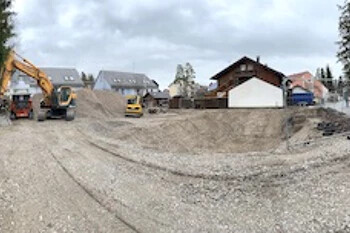 Baustelle mit Baggern und Kieshügeln bei Wohnhäusern, Wolken.