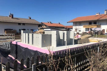 Baustellenfundament mit Betonwänden im Wohngebiet bei blauem Himmel.