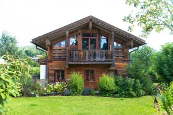 Chalet mit Balkon im Garten, umgeben von Bäumen.