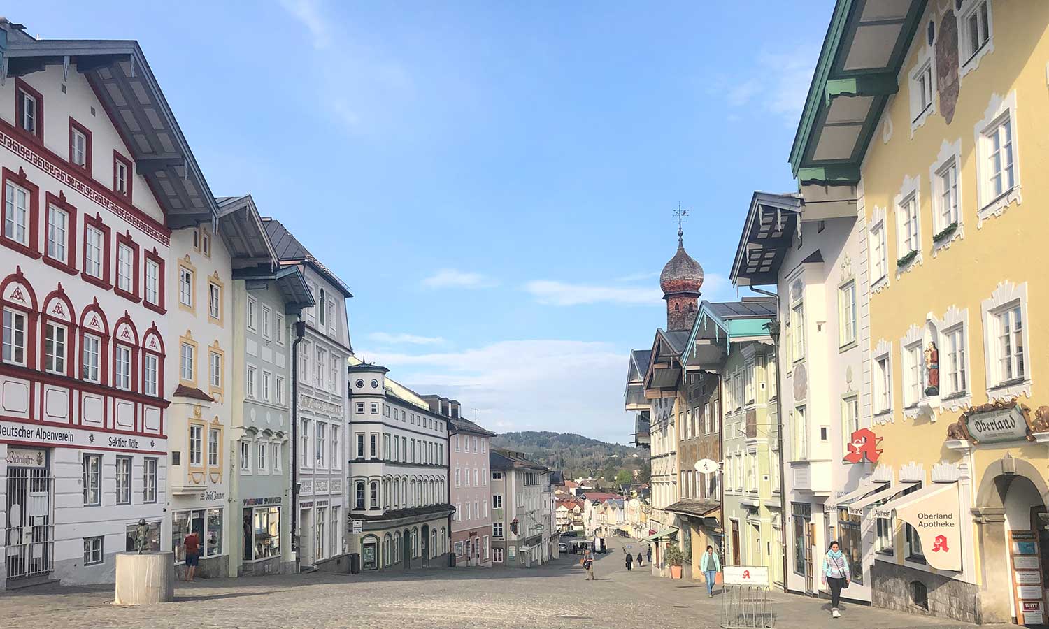 Bunte Altstadthäuser an Kopfsteinpflasterstraße bei blauem Himmel.