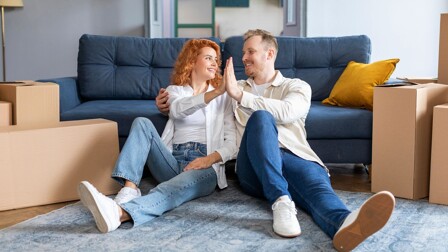 Ein Paar sitzt vor einer Couch und gibt sich ein High-Five.