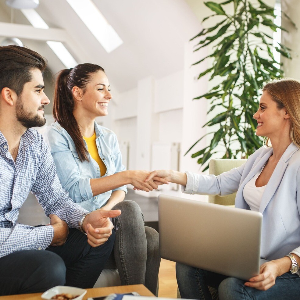 Paar sitzt mit Maklerin zusammen, Frau gibt Maklerin die Hand