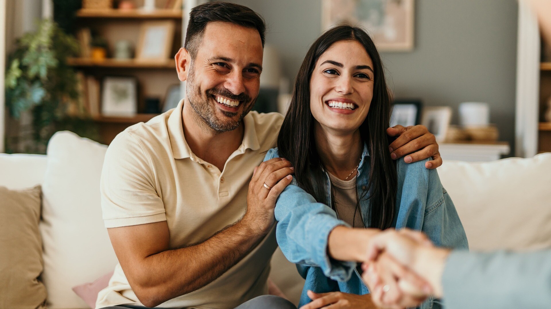 Ein Paar sitzt auf einem Sofa und die Frau schüttelt einer anderen Person die Hand
