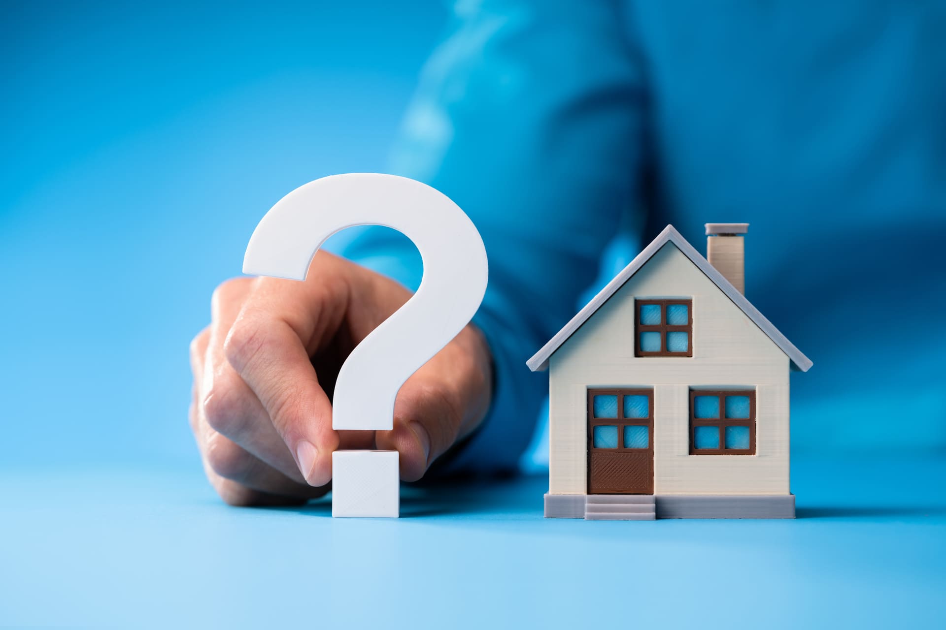 Modellhaus neben einem großen Fragezeichen auf blauem Hintergrund.