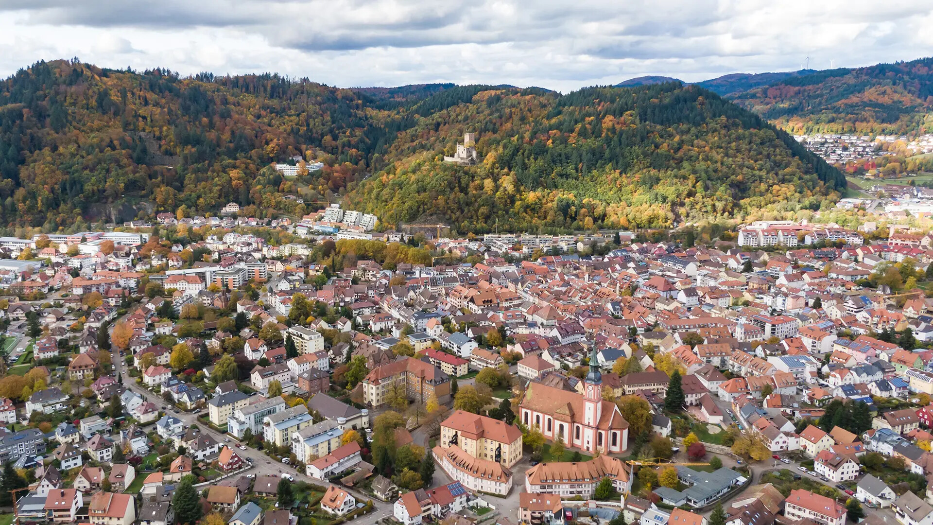 Stadt mit roten Dächern, grünen Hügeln, herbstlichen Farben.