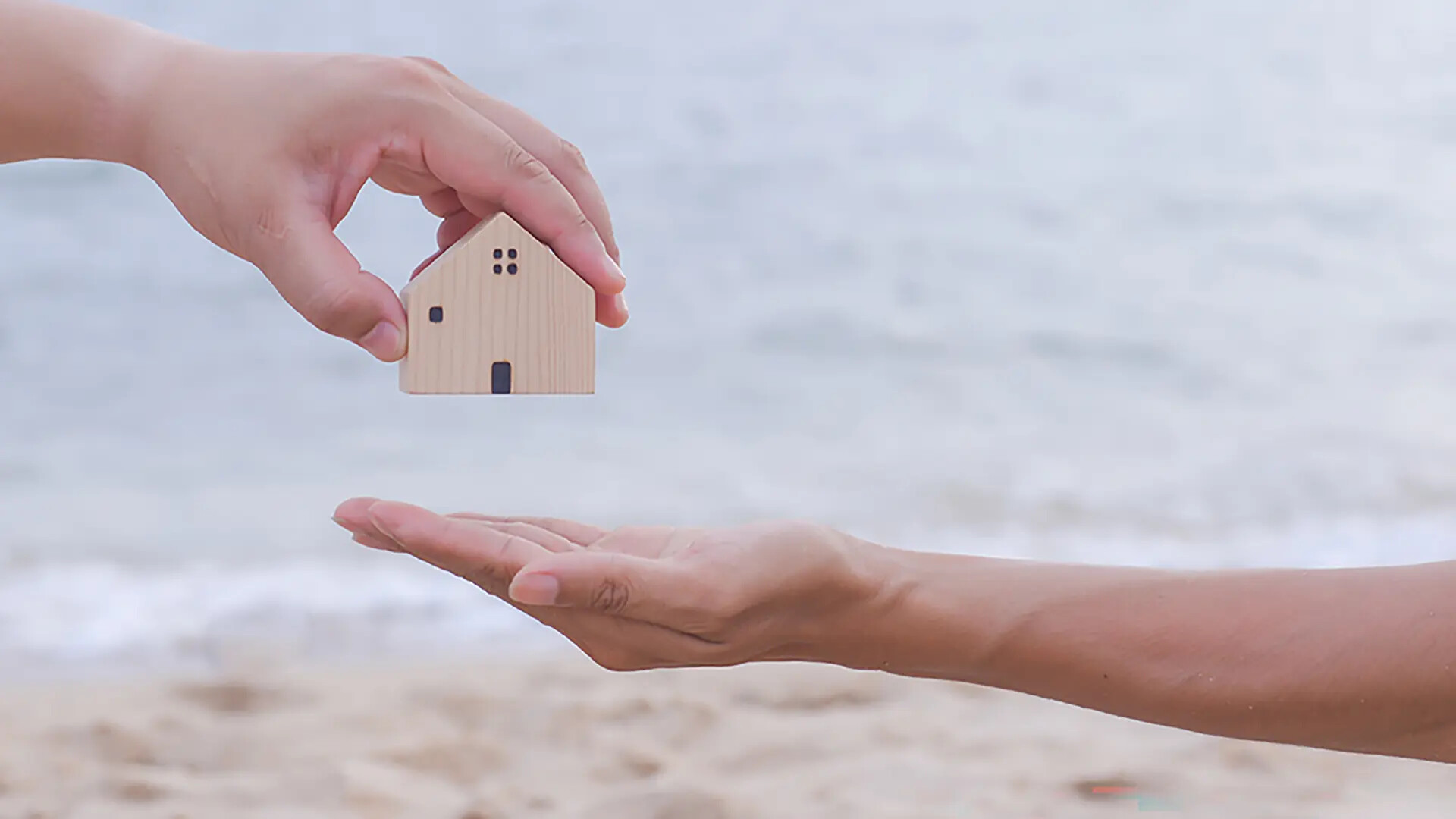 Hände tauschen Holzhaus vor Strand und Meer.