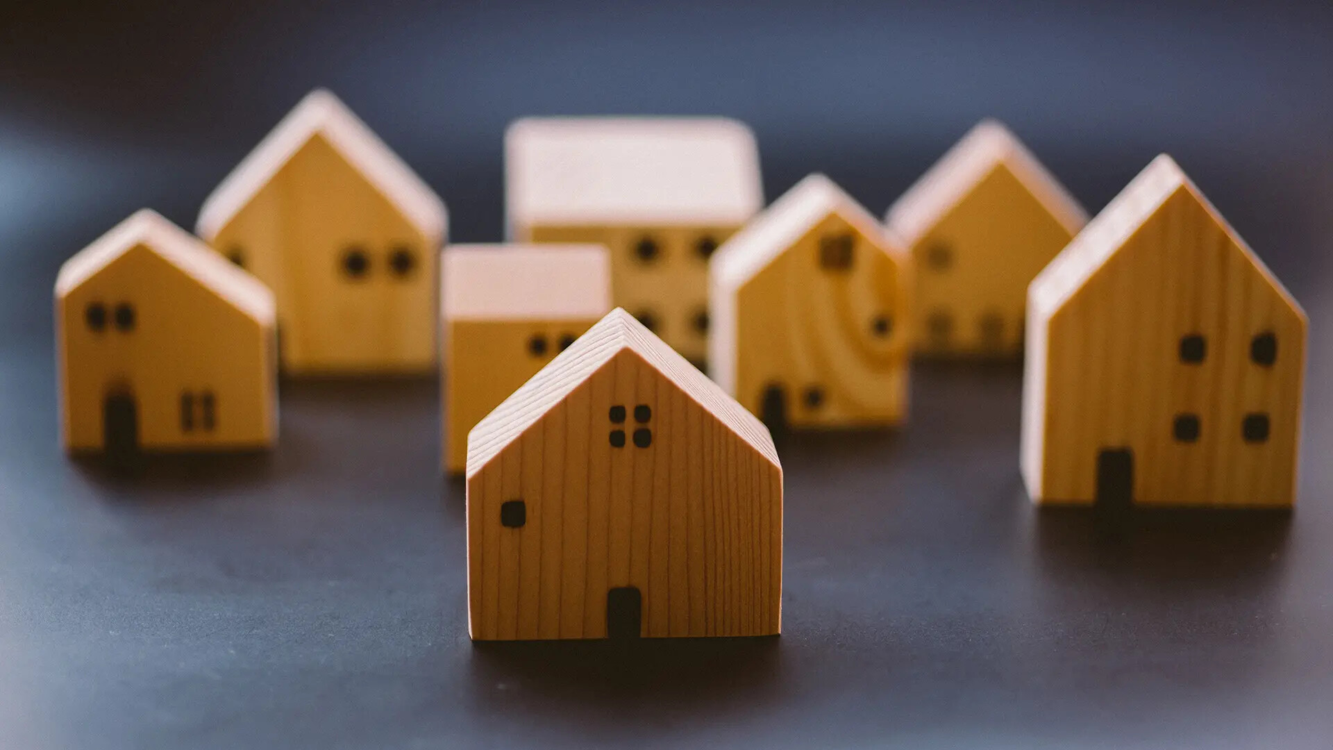 Kleine Holzhaus-Spielzeuge mit schwarzen Fenstern auf dunklem Untergrund.
