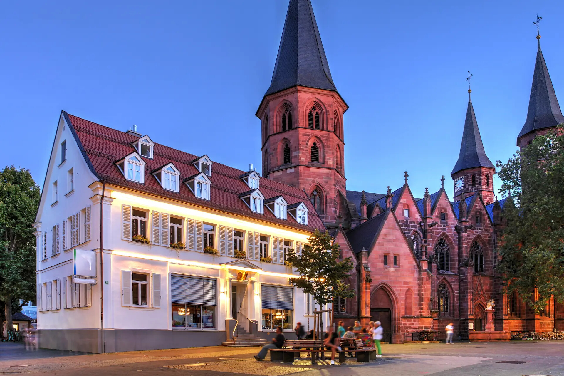 Weiße Kirche mit hohen Türmen, Menschen auf Bänken im Vordergrund.