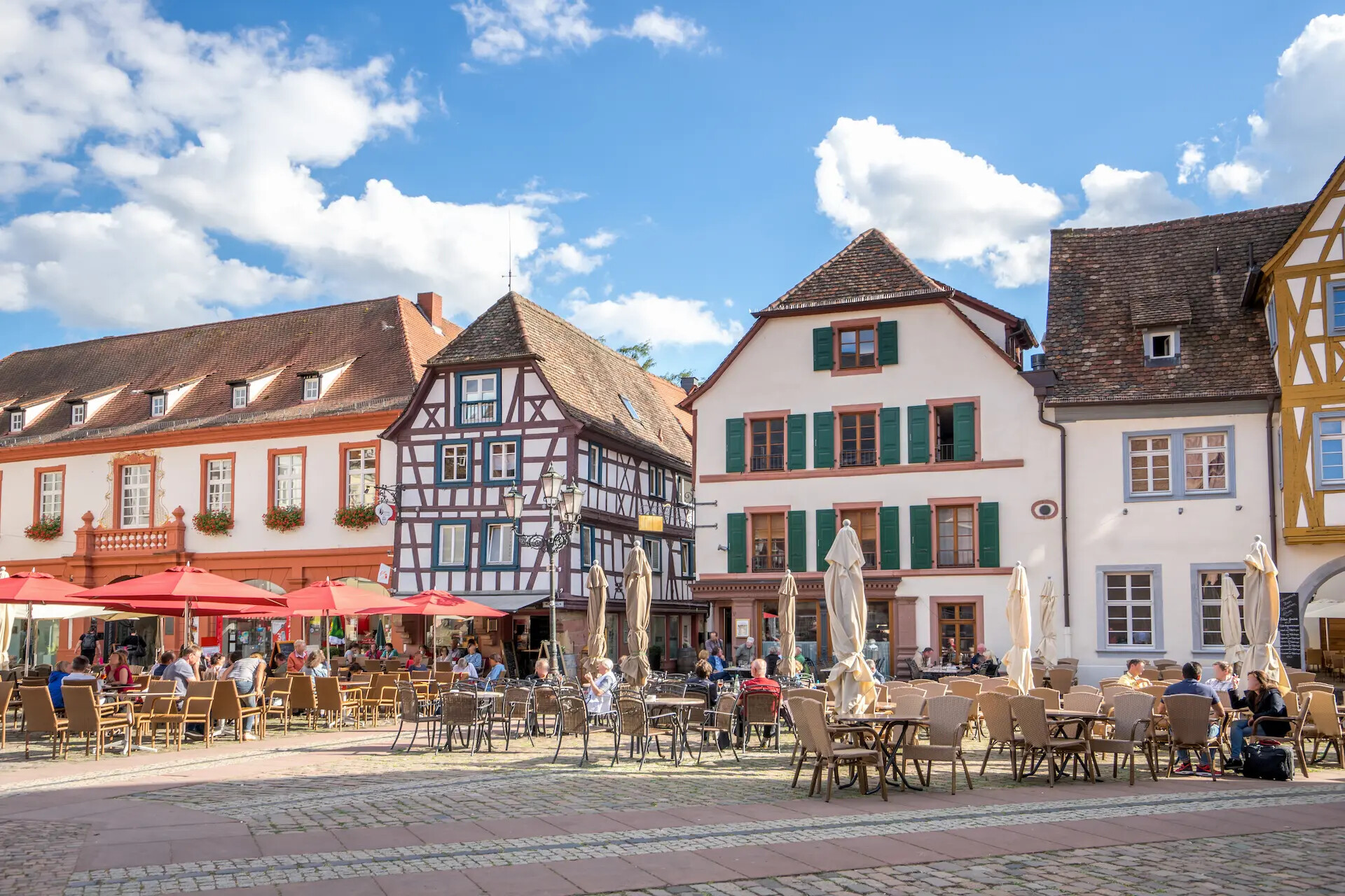 Bunte Fachwerkhäuser und Café-Tische auf sonnigem Platz.