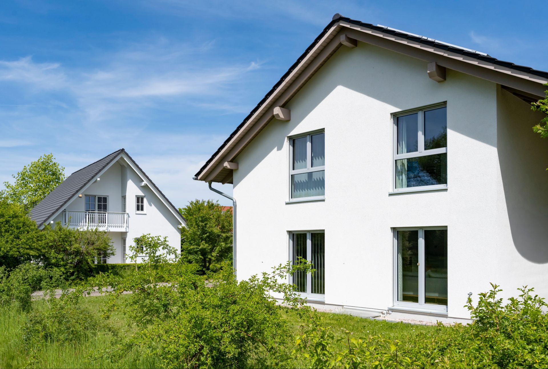 Zwei weiße Einfamilienhäuser mit grüner Natur