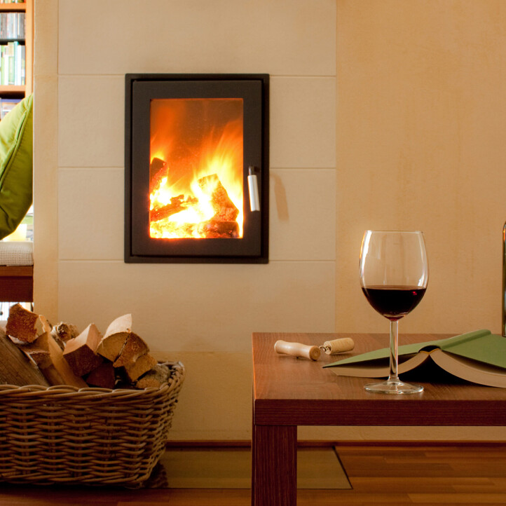 Ein Glas Rotwein, Bücher und Brennholz am Kamin schaffen eine gemütliche Atmosphäre.