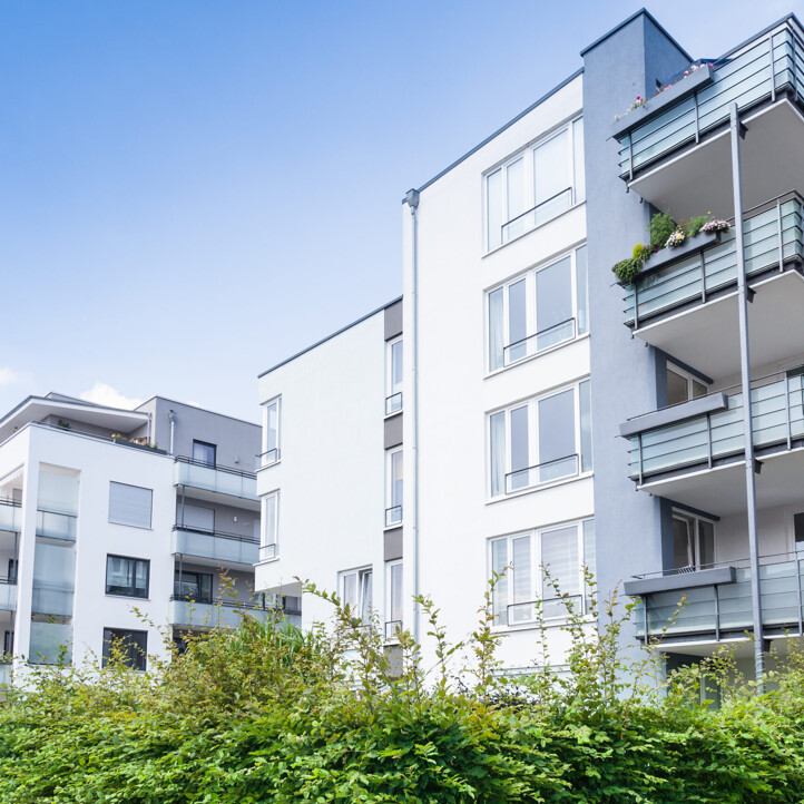 Moderne Mehrfamilienhäuser mit Balkonen und Grünanlagen davor, unter einem klaren blauen Himmel.