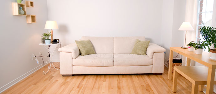 Beigefarbenes Sofa mit grünen Kissen in einem hellen Wohnzimmer mit Holzboden, Pflanzen und Lampen.