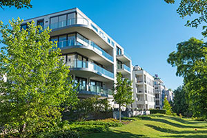 Modernes Mehrfamilienhaus mit Glasbalkonen, umgeben von Bäumen und grünem Rasen unter einem klaren blauen Himmel.