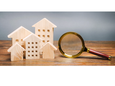 Miniaturhäuser und Lupe auf Holz, symbolisiert Immobiliensuche.