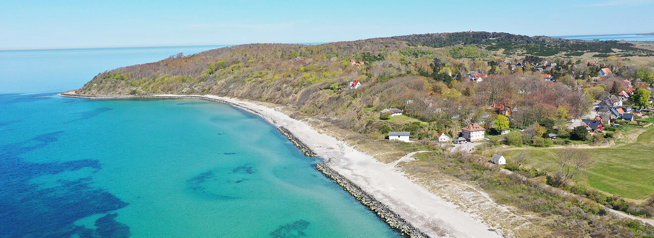 Küste mit blauem Wasser, Sandstrand und Häusern im Grünen.