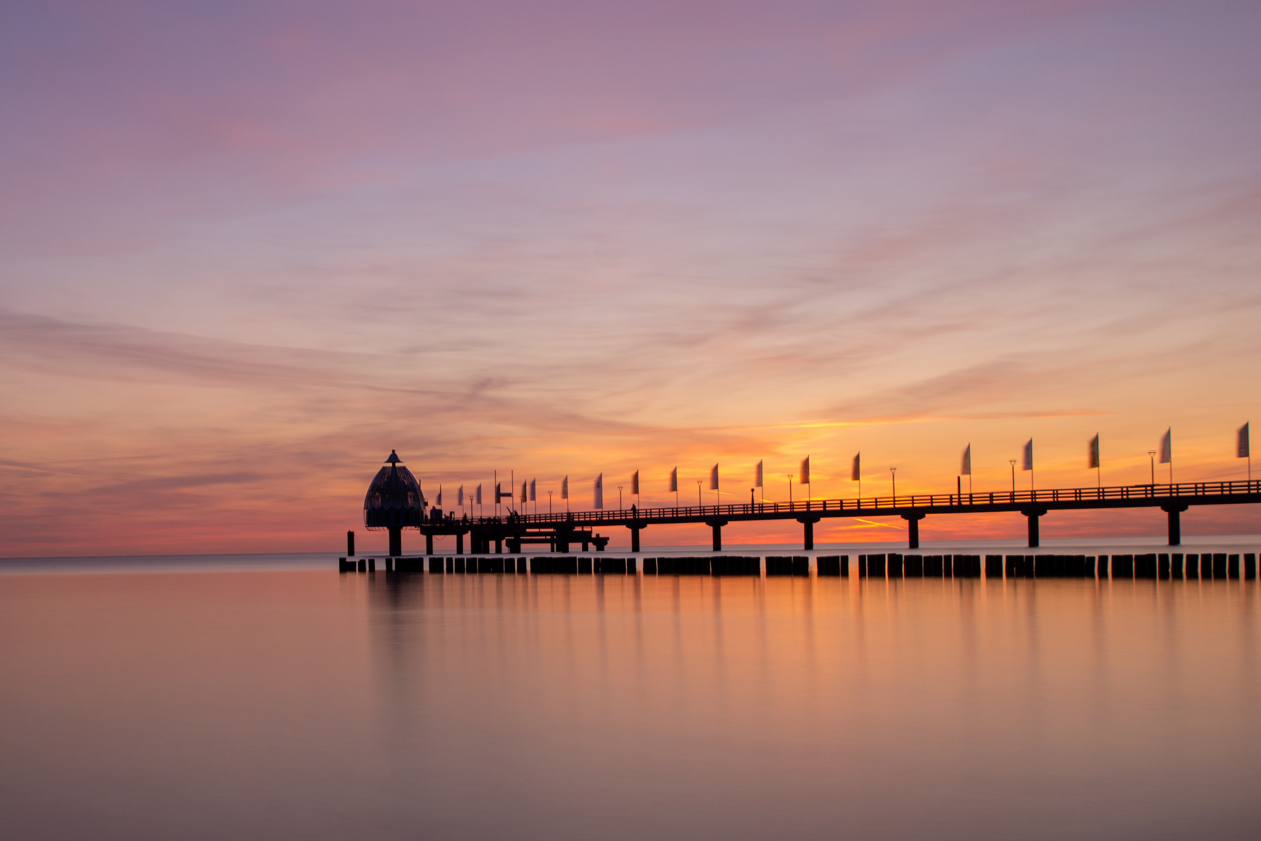 Pier mit Fahnen im Sonnenuntergang, Spiegelung im Wasser.