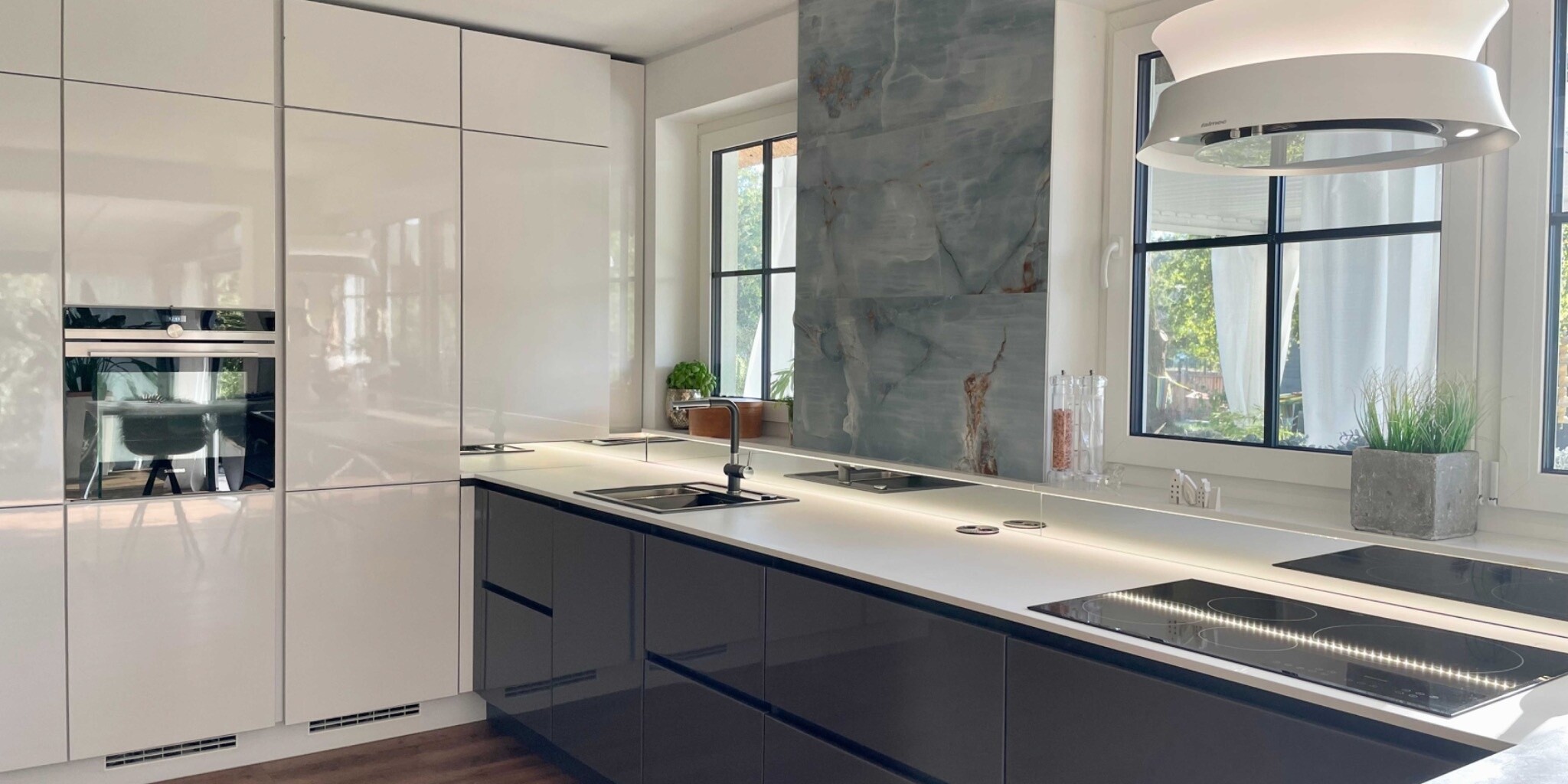 Moderne Küche mit Glanzfronten, Geräten und großen Fenstern.