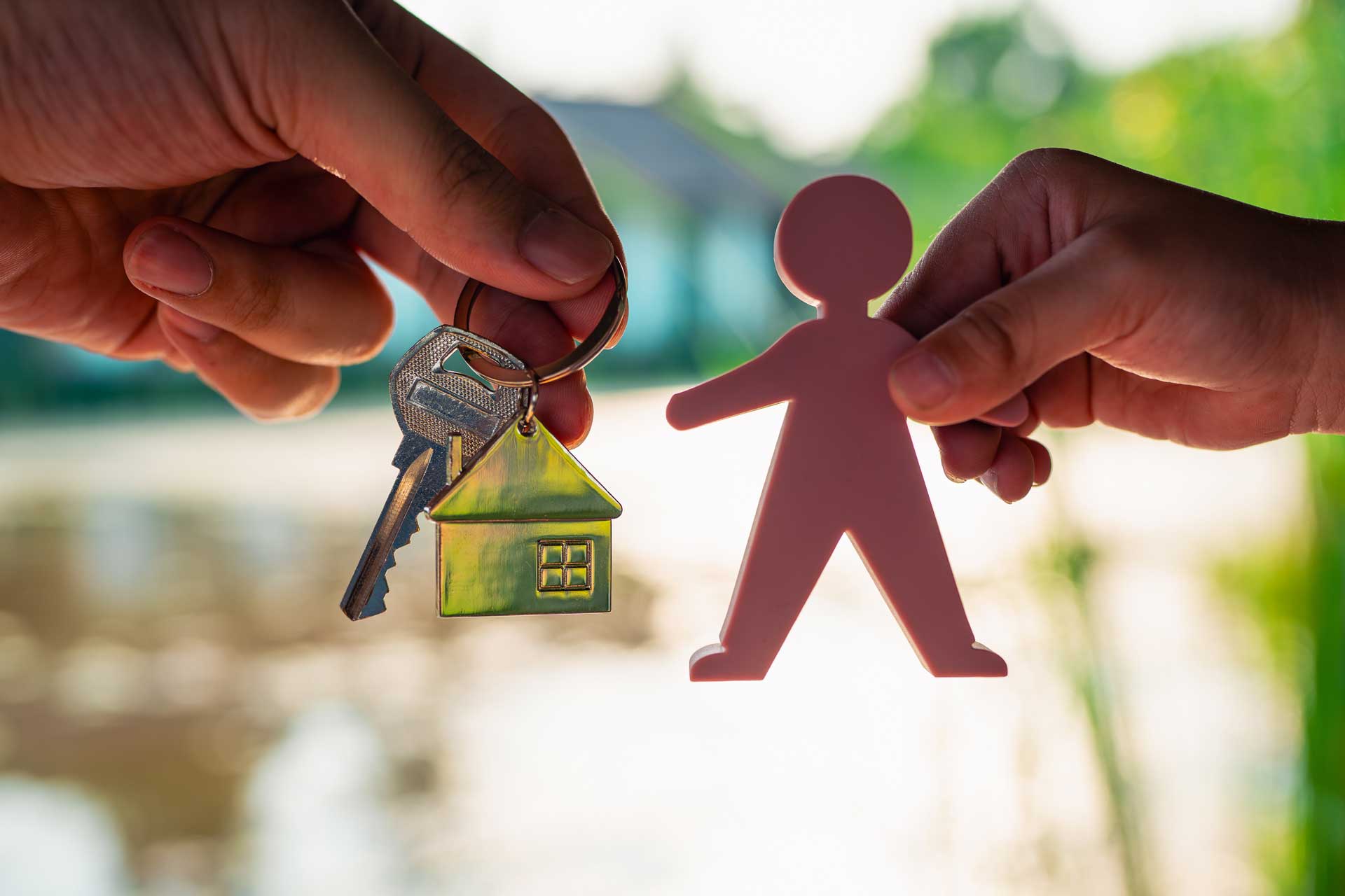 Ältere und jüngere Hand halten Hausschlüssel und kleine Figur in die Kamera als Symbol für Erbimmobilien