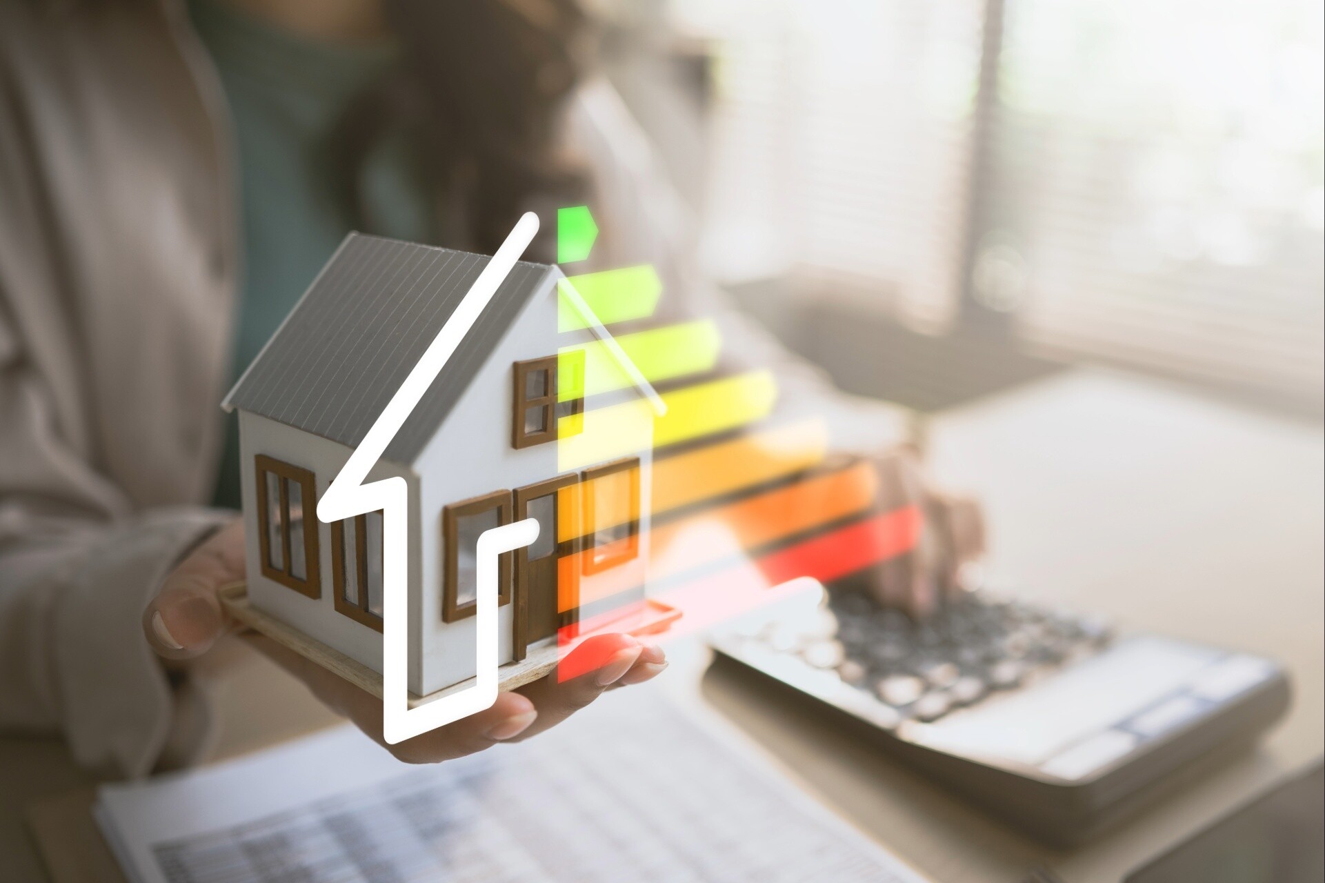 Modellhaus in einer Hand mit einer eingeblendeten Energieeffizienzskala von A bis G.