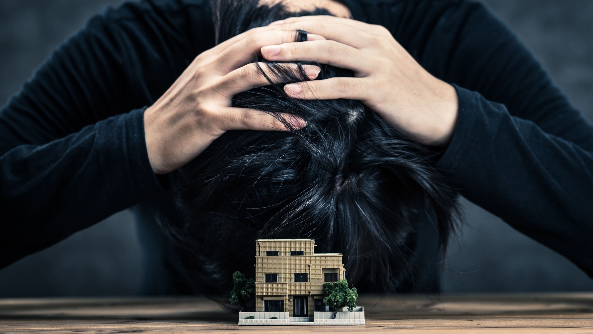 Ein Mensch legt verzweifelt den Kopf auf den Tisch, davor ein kleines Modellhaus