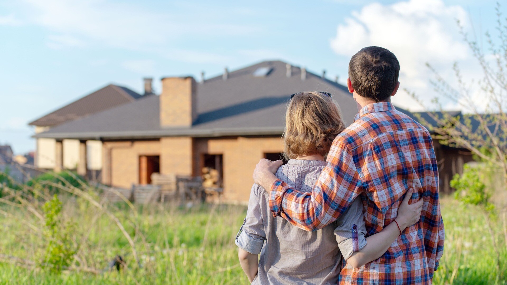 Paar steht Arm in Arm und schaut in Richtung eines Hauses