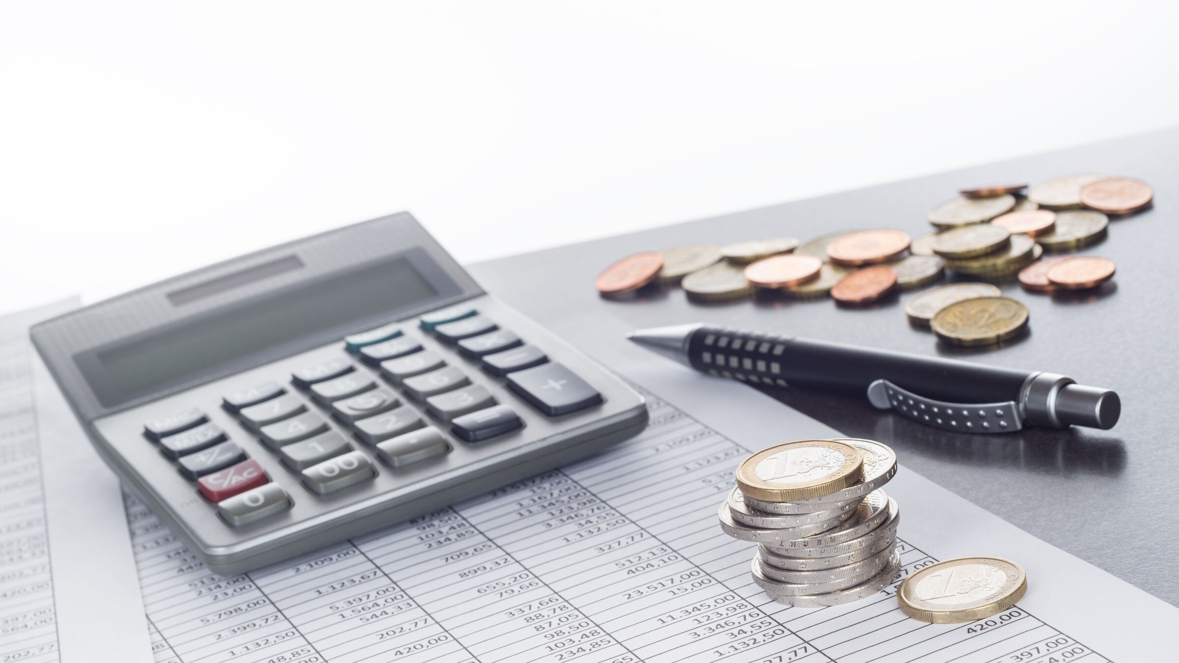 Taschenrechner liegt neben einem Kugelschreiber und diversen Münzen