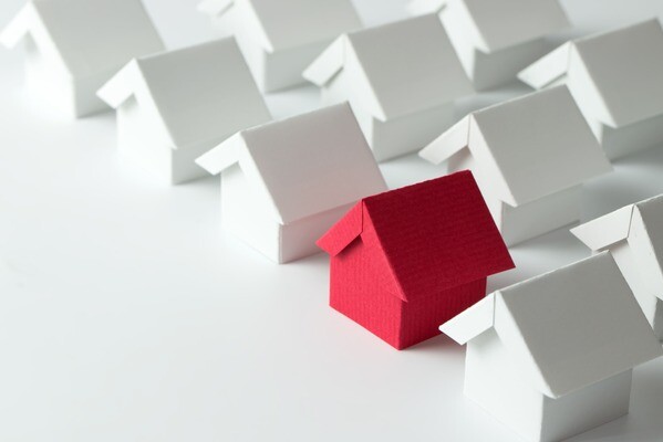 Mehrere Papierhäuser stehen nebeneinander, alle sind weiß bis auf eines, das ist rot