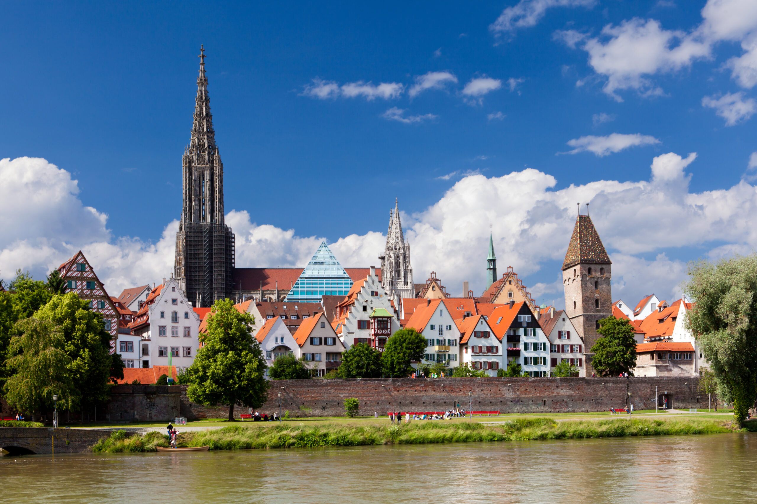 Bunte Häuser und Kirchtürme am Fluss in Ulm bei blauem Himmel.
