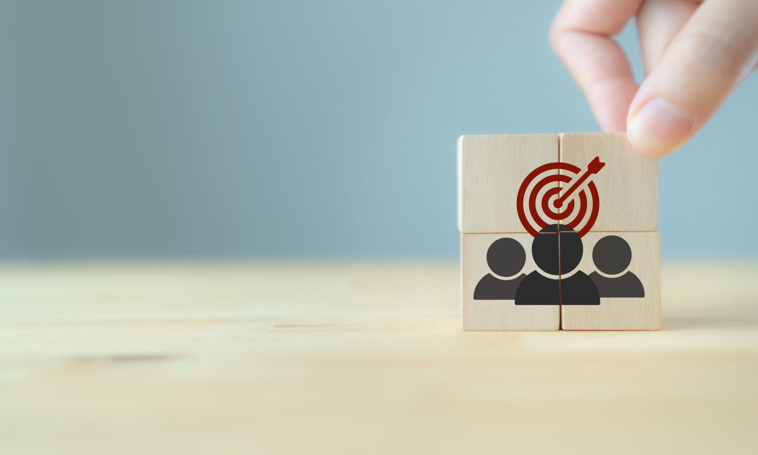 Hand stellt Holzklötze mit Personen-Icons und Zielscheibe auf.