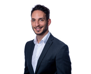 Mann im dunklen Anzug und weißem Hemd lächelt vor Weiß.