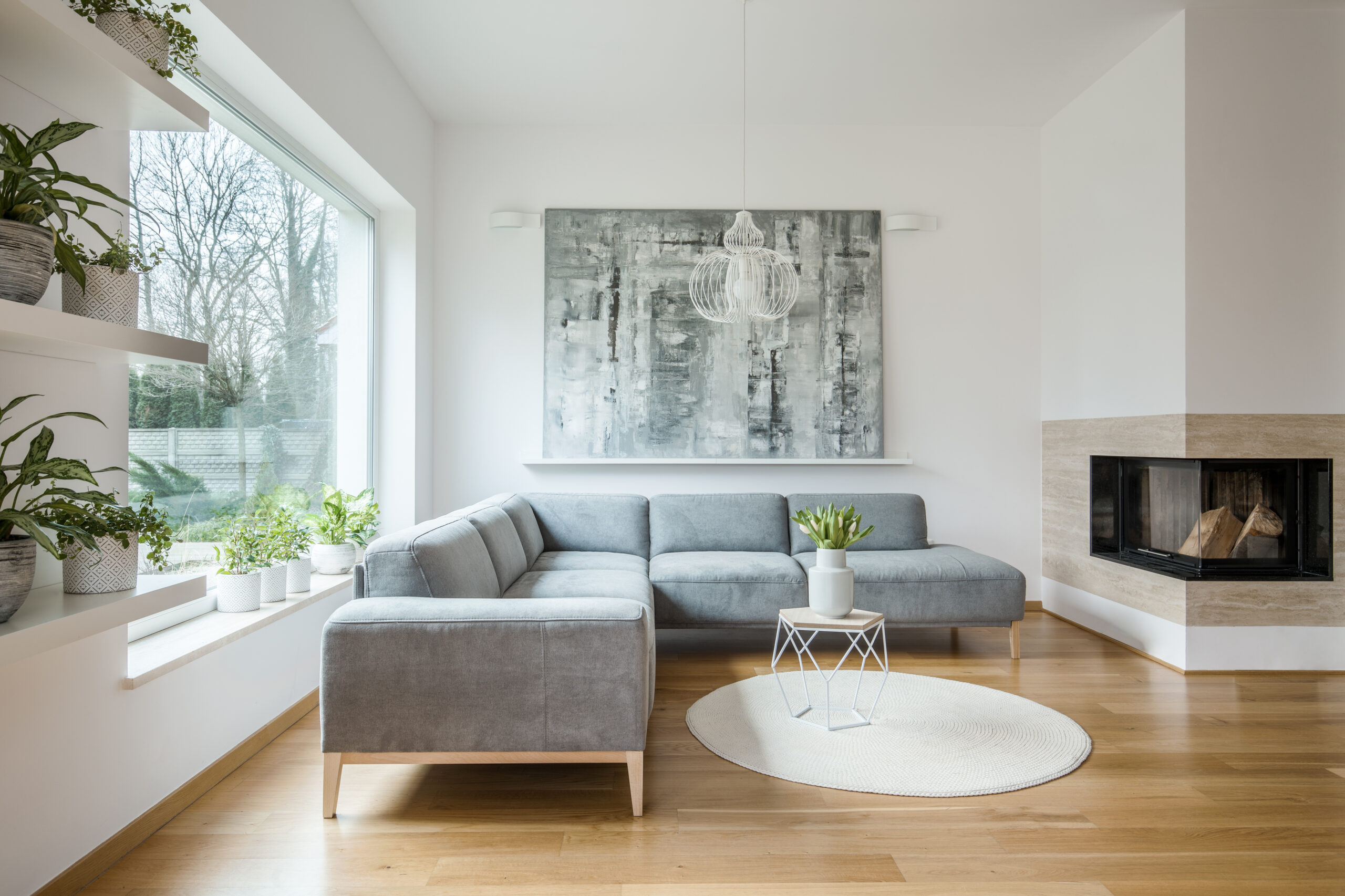 Graues Sektionssofa, großes Fenster, Pflanzen, Kunst und Kamin.