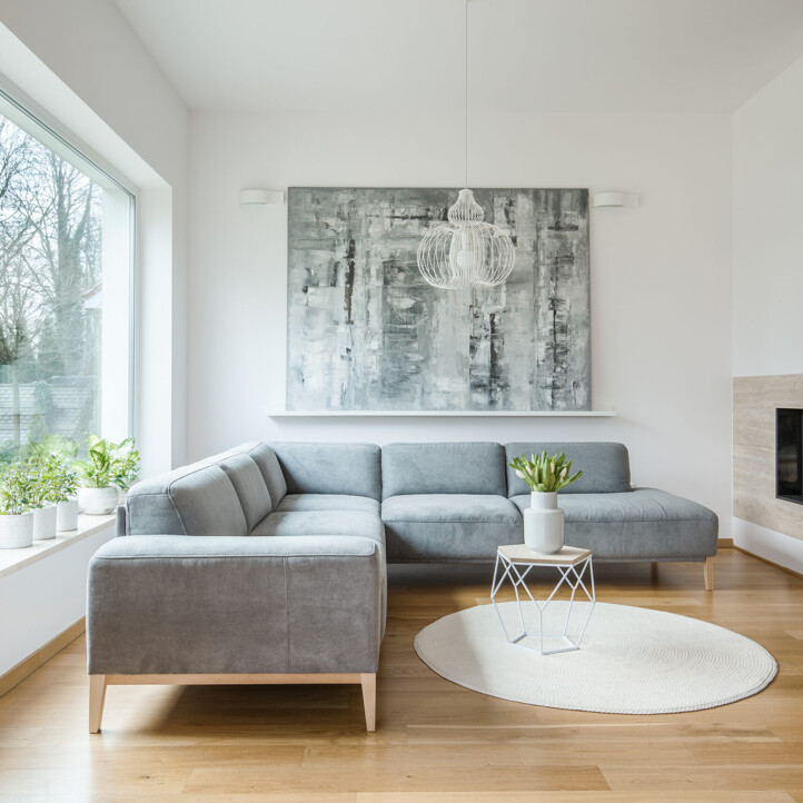 Graues Sofa, Pflanzen, großes Fenster, Kamin, abstrakte Kunst.