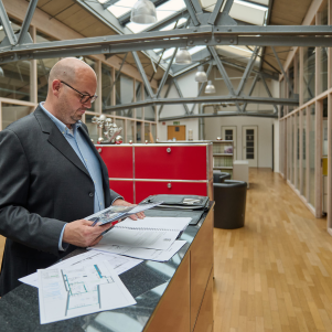 Glatzköpfiger Mann im Anzug prüft Dokumente im modernen Büro.