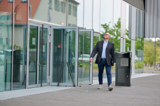 Mann in Blazer und Jeans vor modernem Glasgebäude, blickt hoch.