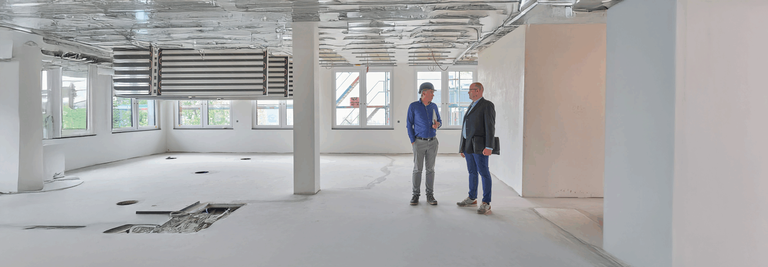 Zwei Männer sprechen in einem unfertigen Raum mit offenen Decken.