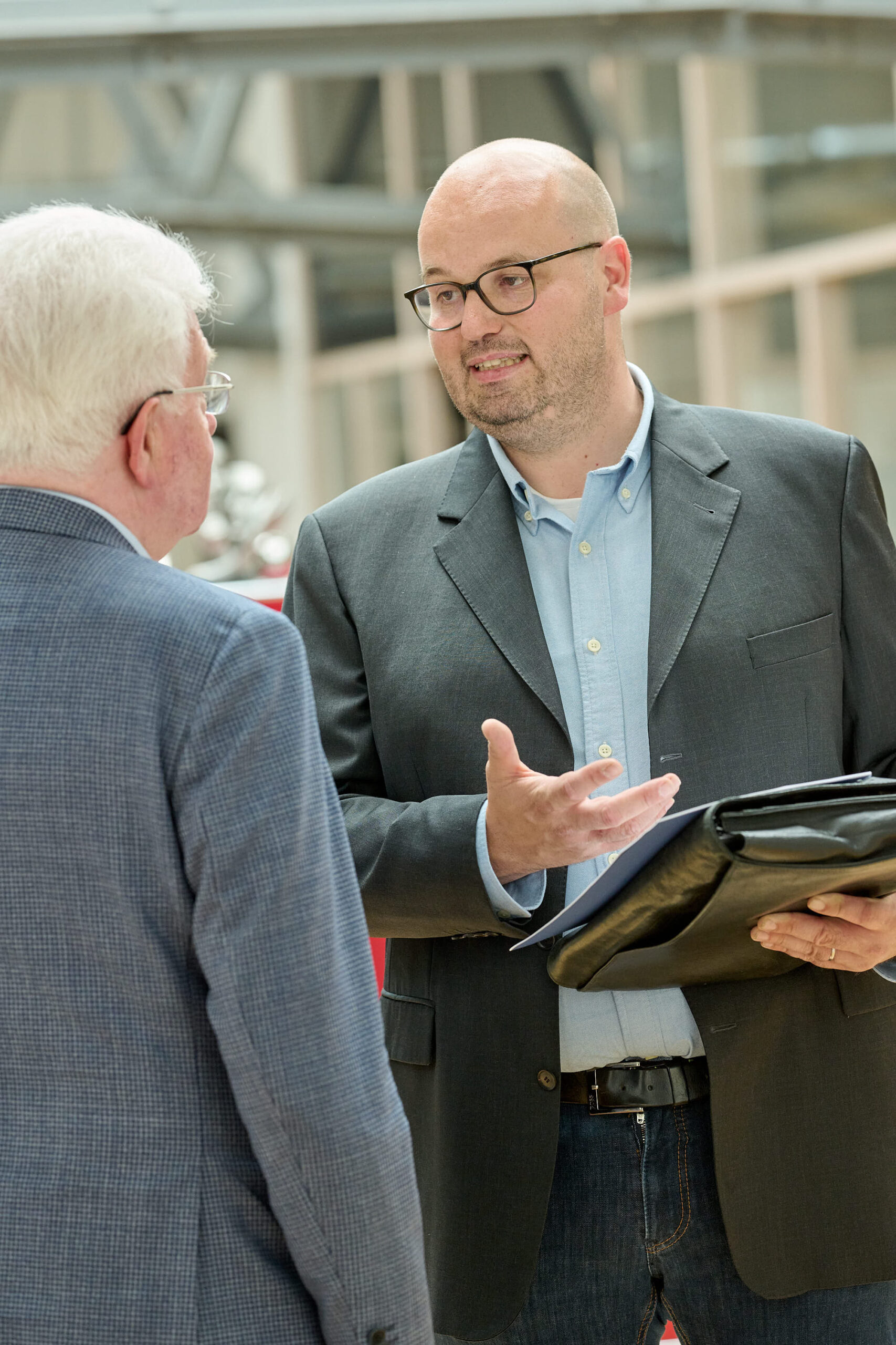 Zwei Männer im Anzug sprechen, einer hält eine Mappe.