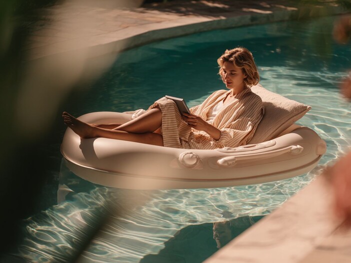 Frau liest auf Pool-Schwimmreifen in der Sonne ein Buch.