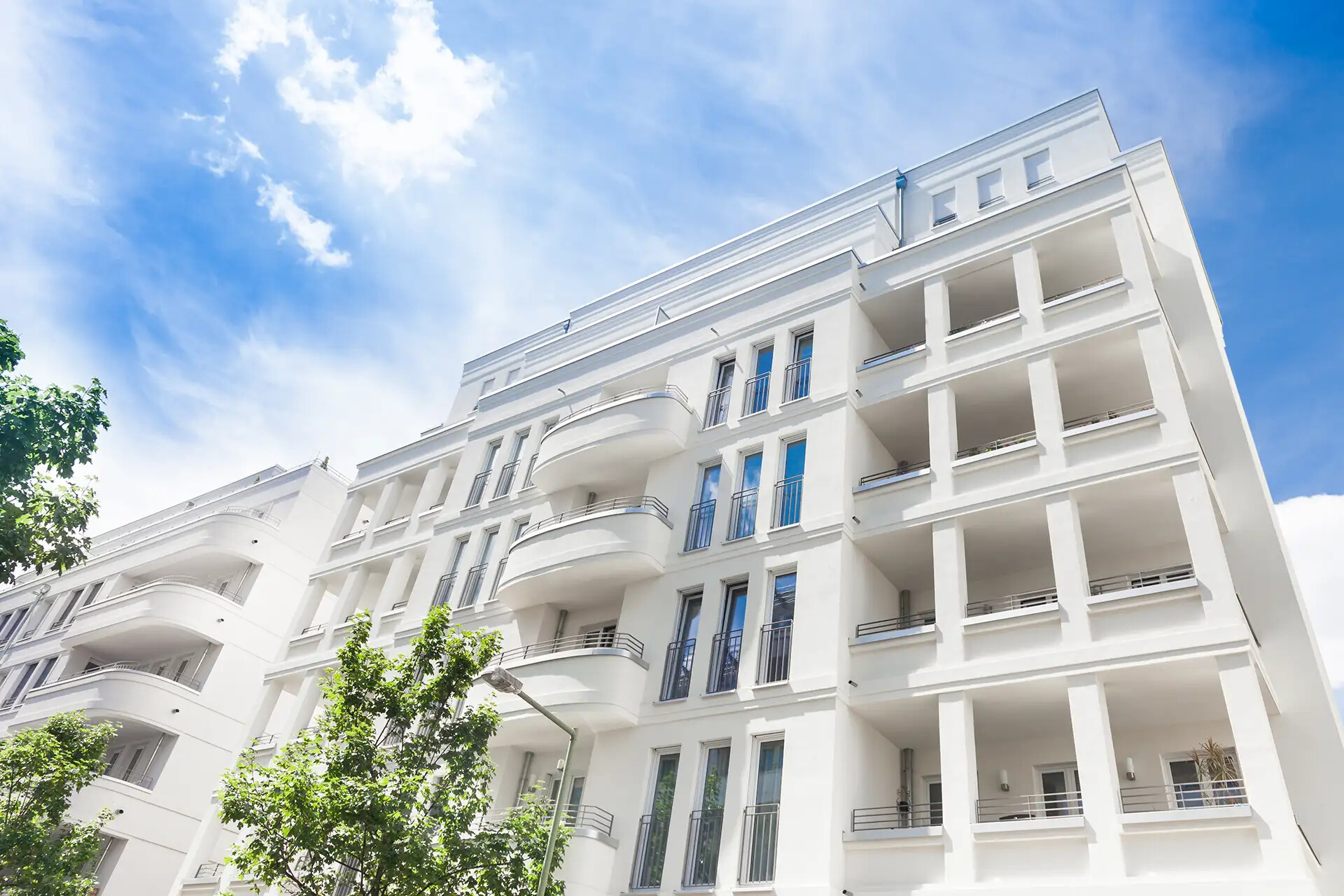 Modernes weißes Wohnhaus mit Balkonen und großen Fenstern.