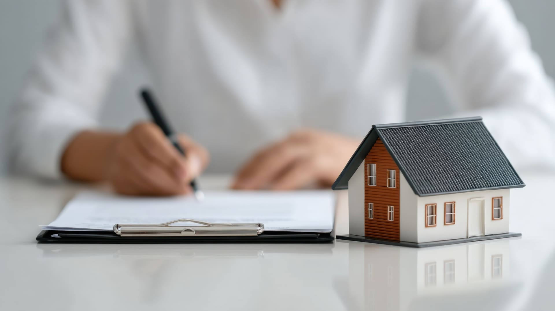 Immobilienmakler prüft Vertragsunterlagen neben Modellhaus im modernen Büro.