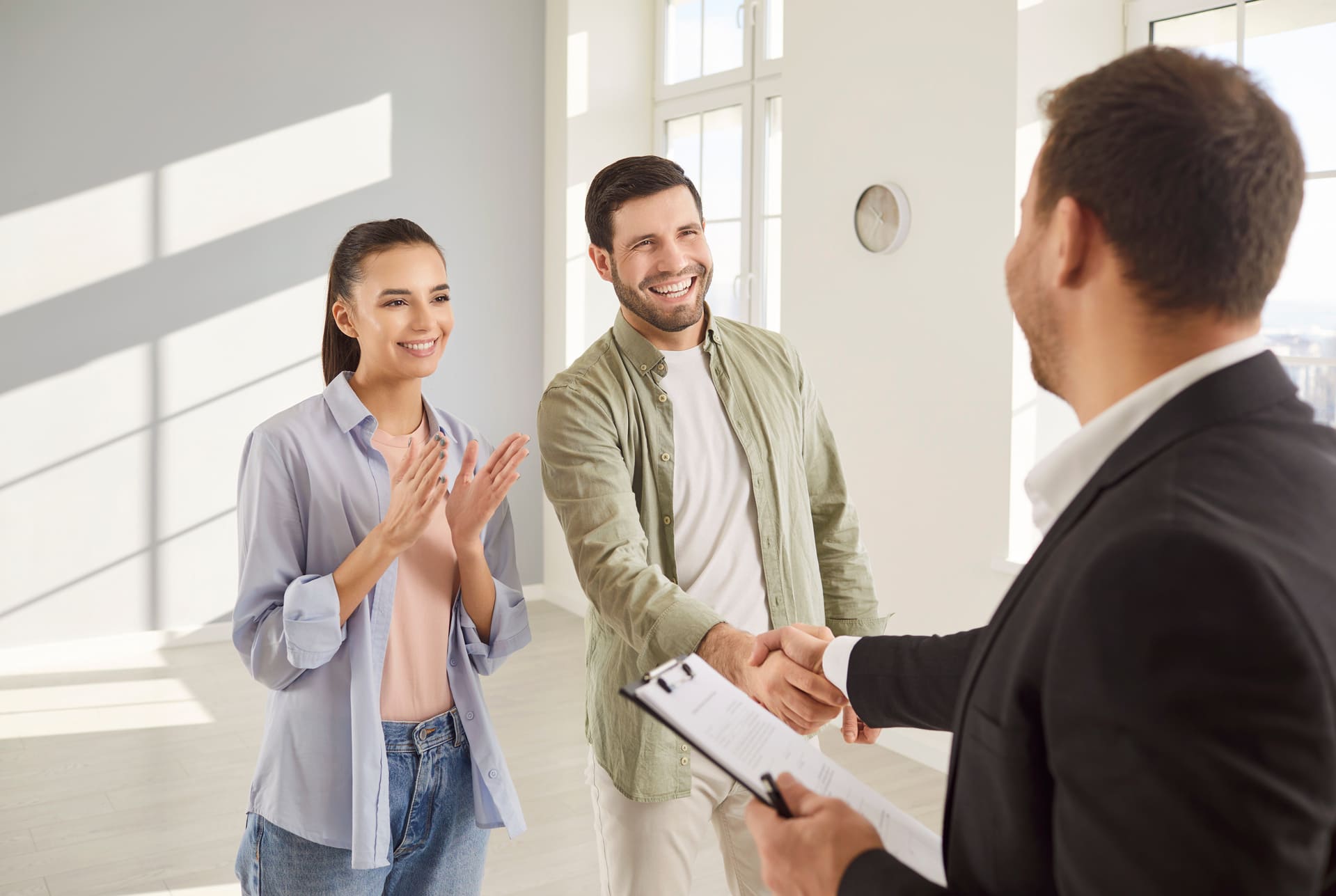 Handschlag zwischen jungem Paar und Immobilienmakler zum Vertragsabschluss.