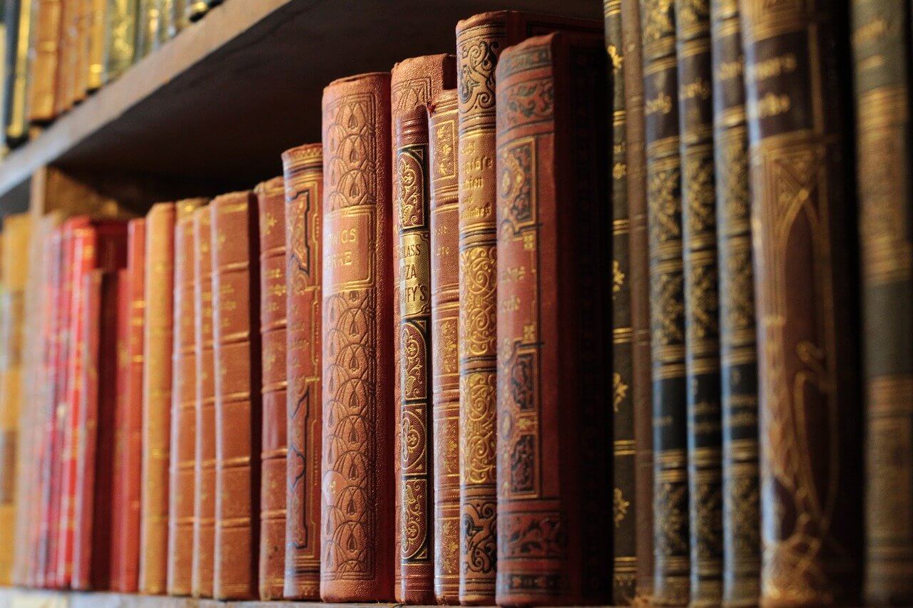 Antike Bücher mit verschnörkelten Buchrücken auf einem hölzernen Bücherregal.