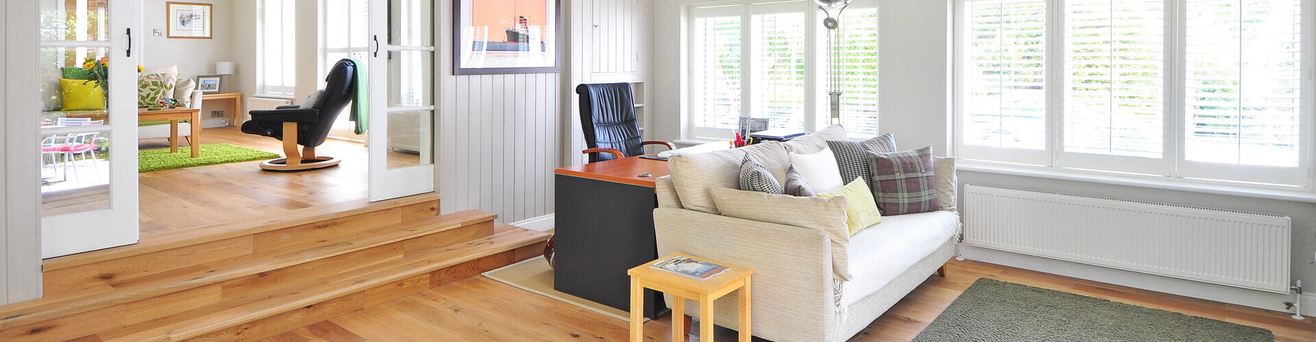 Helles Wohnzimmer mit Holzboden, cremefarbenem Sofa und Fenstern.