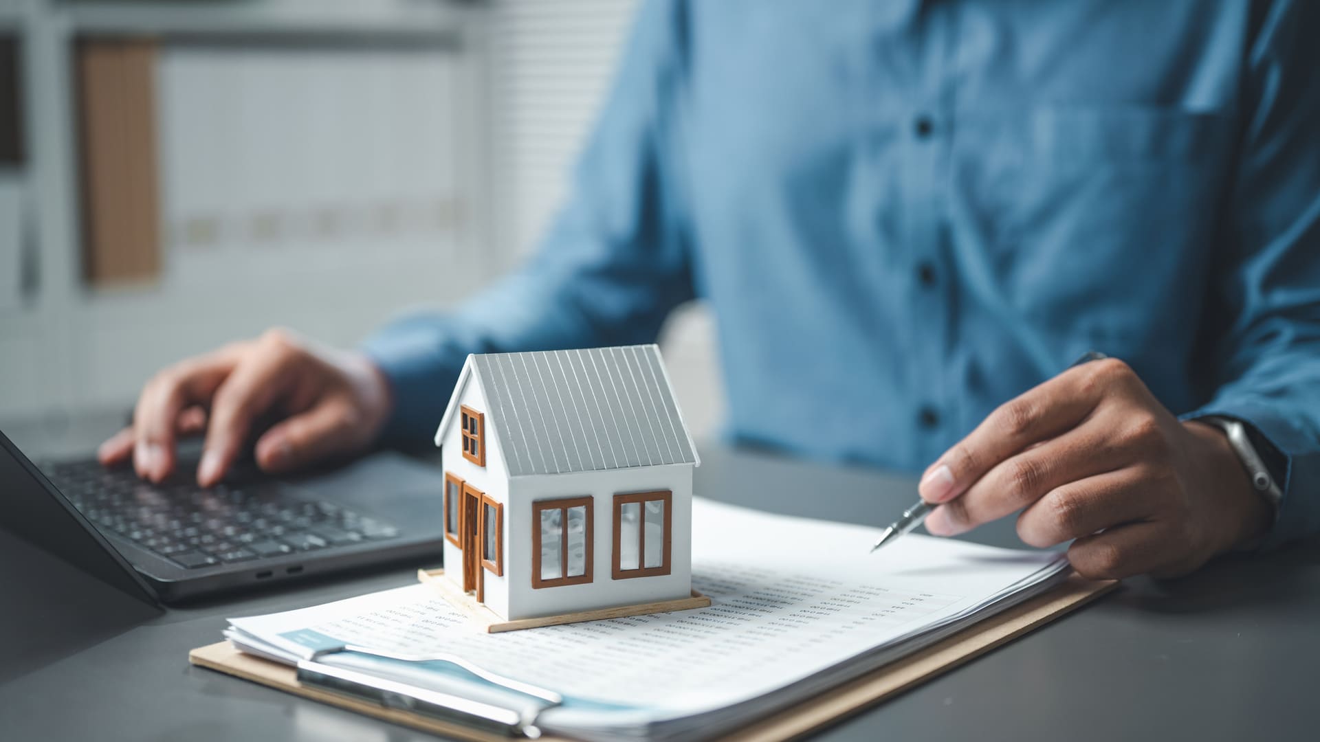 Modellhaus auf Unterlagen während Person Dokumente zu Immobilien prüft.