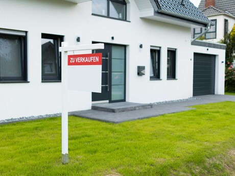 Zu Verkaufen-Schild auf dem Rasen vor einem Einfamilienhaus