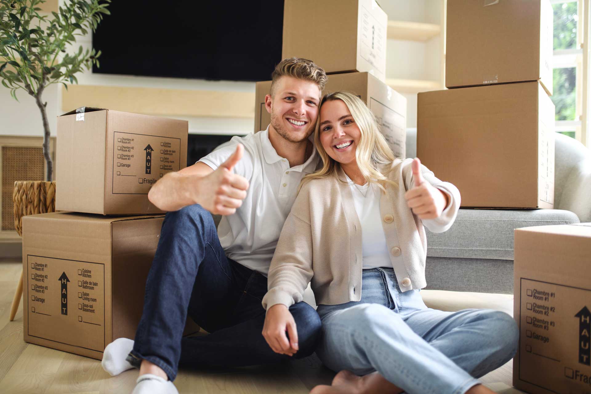 Junges Paar hat sich das erste Haus gekauft und zeigt Daumen hoch in die Kamera