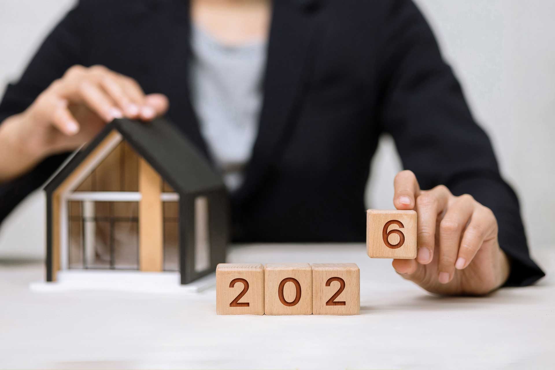 Maklerin mit Modellhaus und Holzwürfeln mit der Zahl 2026: Neues in der Branche