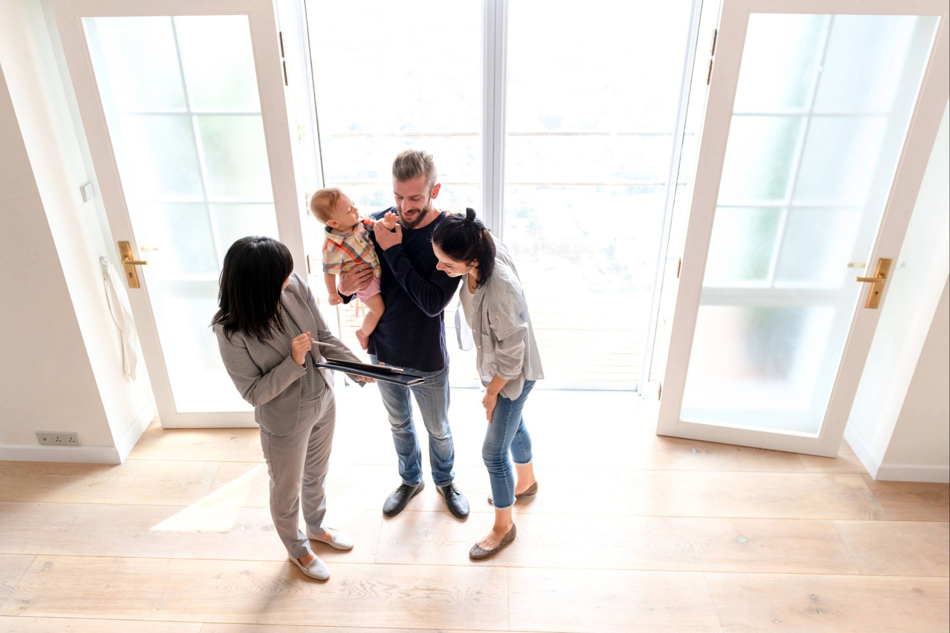 Junges Paar mit Kleinkind besichtigt helle Neubauwohnung mit Immobilienmaklerin.